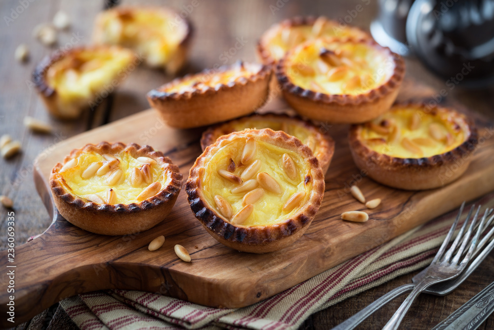 Homemade custard tarts with pine nuts on rustic wooden cutting board