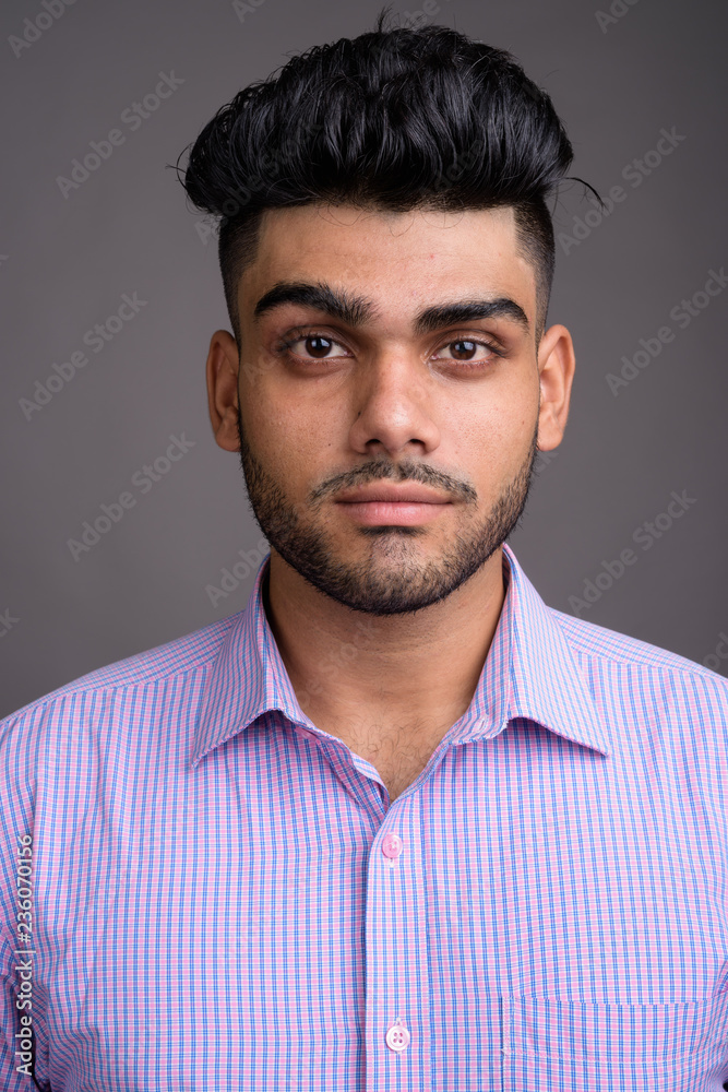 Young handsome Indian businessman against gray background