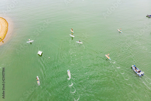 Strong men floating on a SUP boards in a beautiful bay on a sunny day. Aerial view of the men crosses the bay using the paddleboard. Water sports, competitions photo