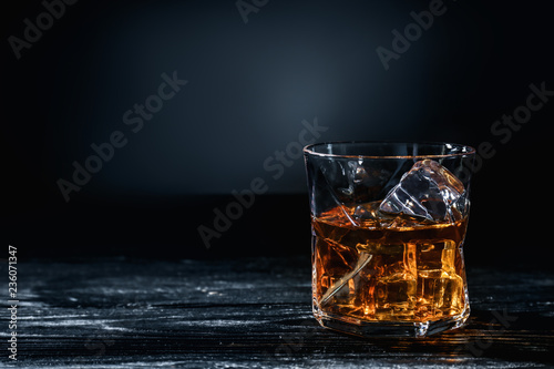 Print op canvas Glass of whisky with ice on wooden table against dark background