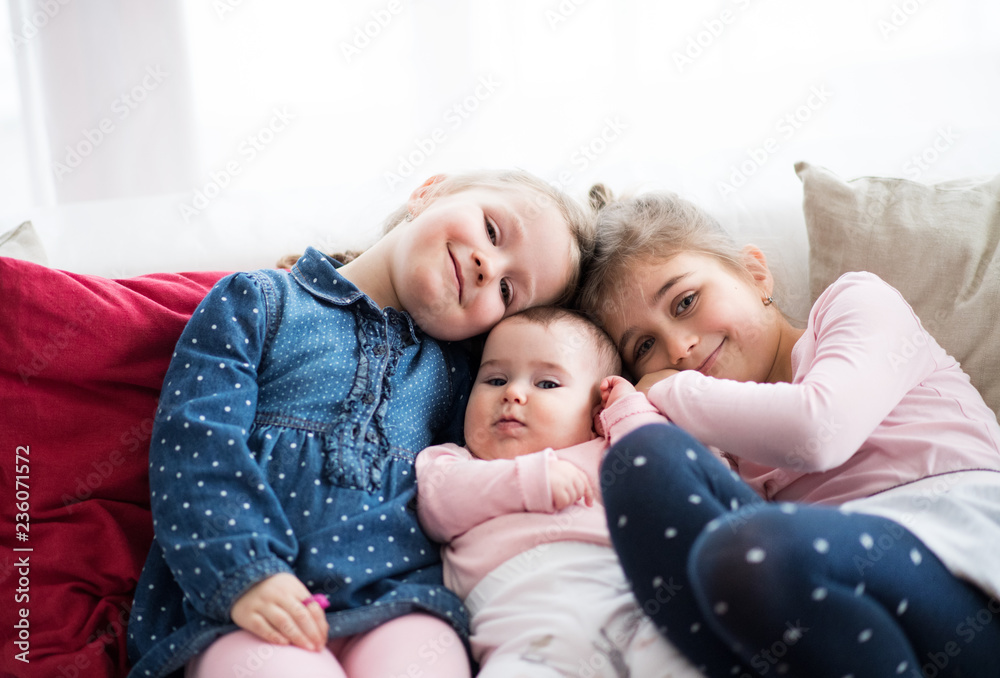 A portrait of three small girls sitting indoors on a sofa. A portrait of three small girls sitting indoors on a sofa.