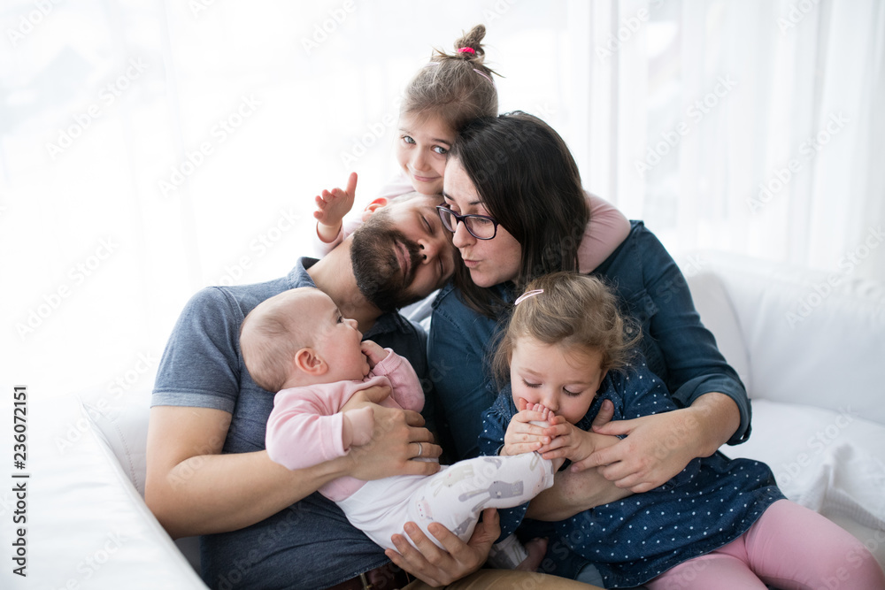 A portrait of young family with small children sitting indoors on a sofa, having fun. A portrait of young family with small children sitting indoors on a sofa, having fun.