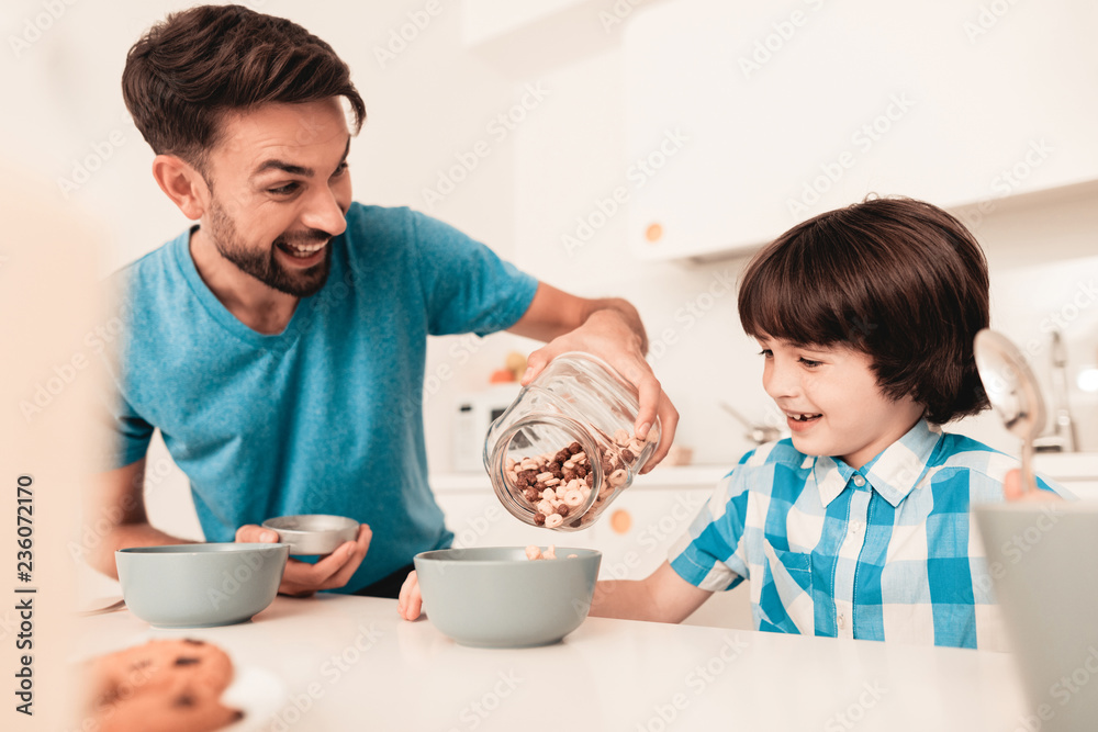 Smiling Son and Father Have Breakfast in Kitchen. Smiling Son and Father Have Breakfast in Kitchen.