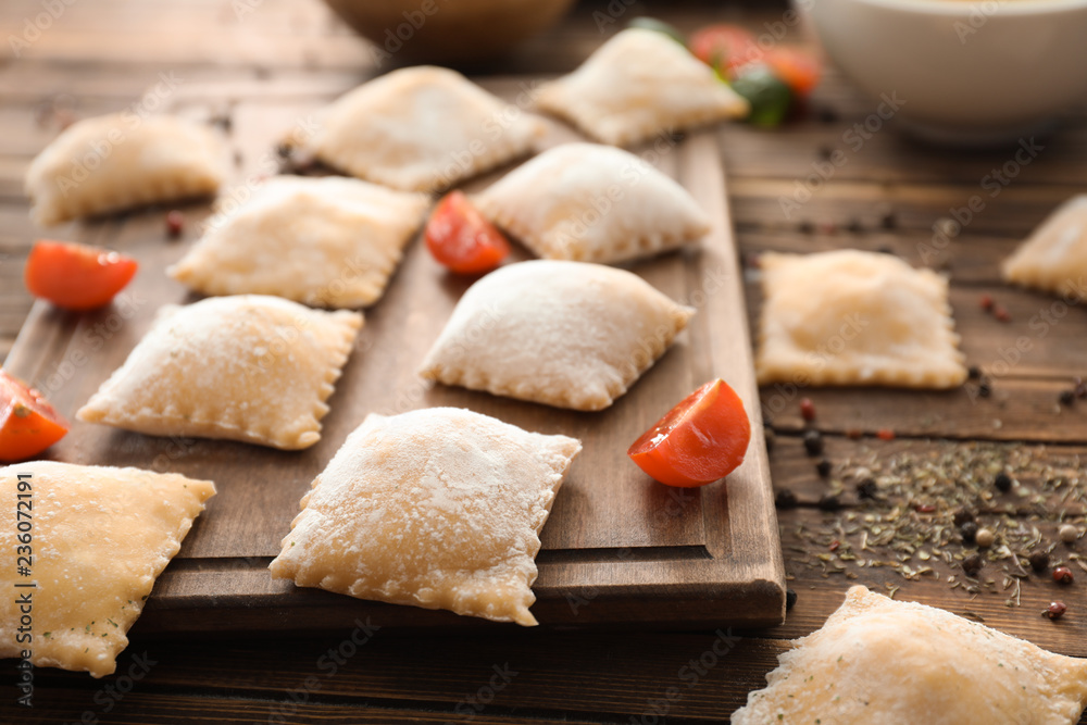 Board with uncooked ravioli on wooden table