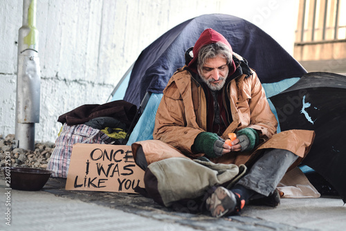 Homeless beggar man sitting outdoors in city asking for money donation. photo