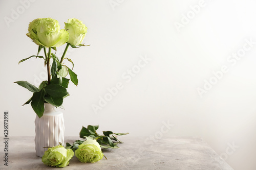 Vase with beautiful bouquet of green roses on table against light background