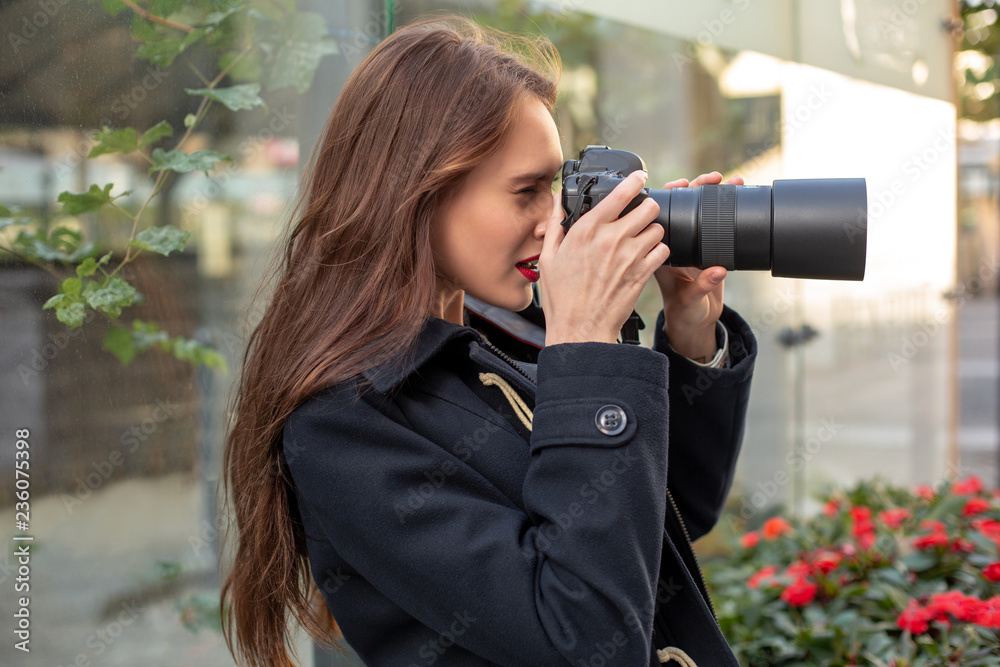 Portrait of professional female photographer on the street photographing on a camera.