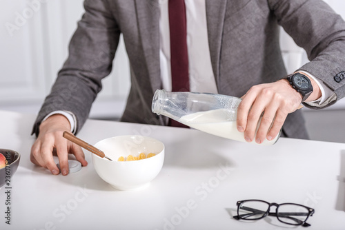 cropped view of businessman pouring milk in cereal bowl at kitchen table