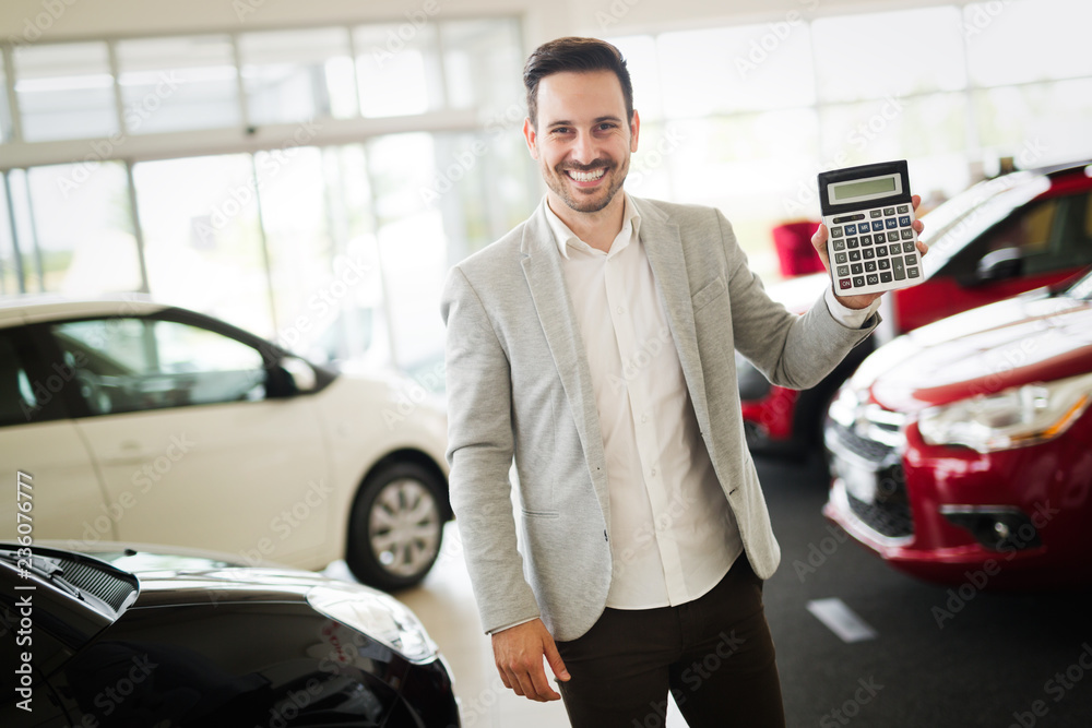 Young attractive salesman is holding a calculator and pointing at incredibly nice price for a car Young attractive salesman is holding a calculator and pointing at incredibly nice price for a car