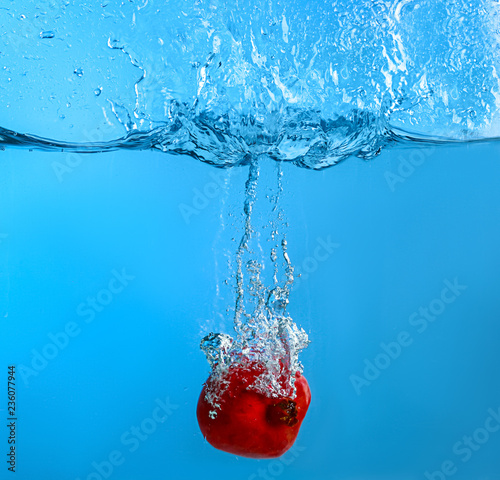 Falling of pomegranate into water on color background
