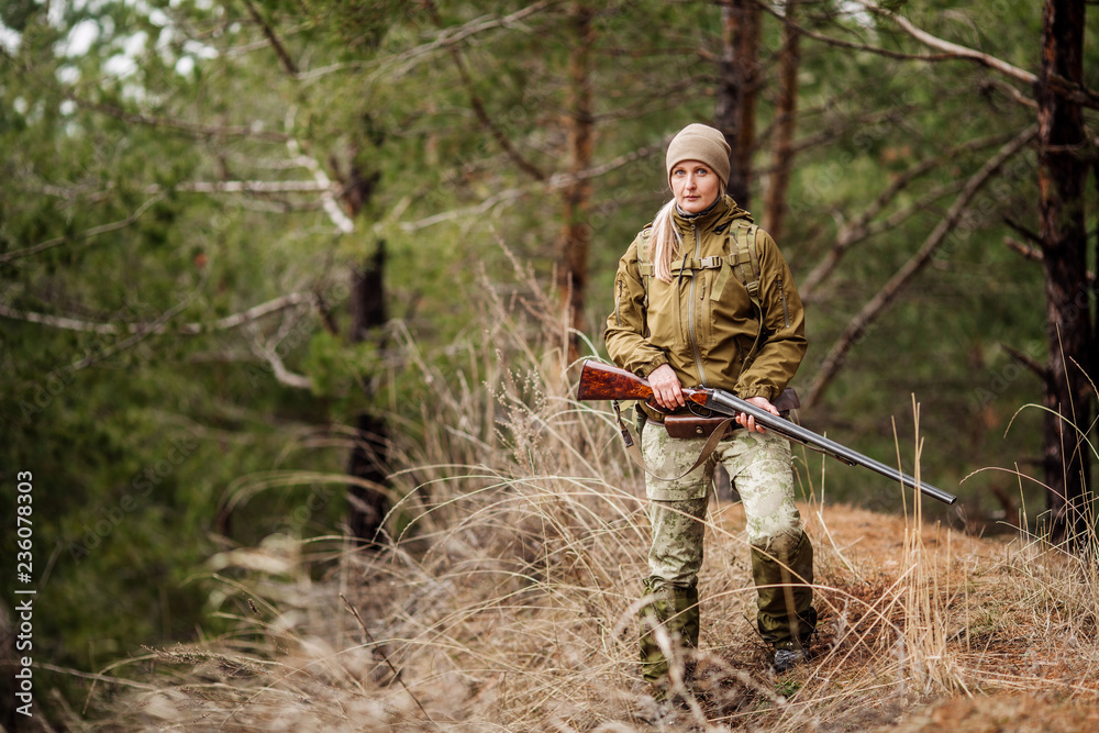 Female hunter in camouflage clothes ready to hunt, holding gun and walking in forest. Female hunter in camouflage clothes ready to hunt, holding gun and walking in forest.