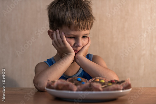boy sits at the table and looks at the plate with cookies