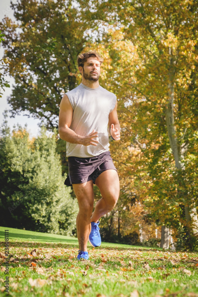 Closeup of one young athlete man running on the grass in the park during autumn. Closeup of one young athlete man running on the grass in the park during autumn.