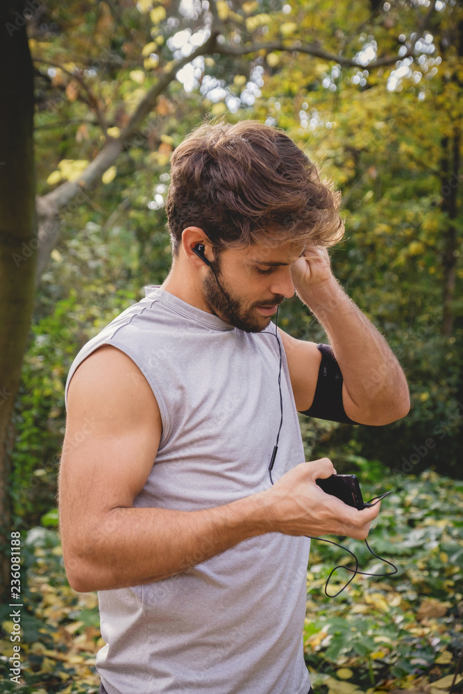Closeup of one young athlete man preparing his smart phone on a path in the park during autumn. Closeup of one young athlete man preparing his smart phone on a path in the park during autumn.