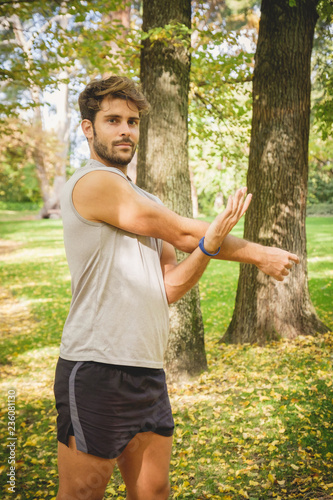 Closeup of one young athlete man stretching on the grass in the park during autumn.