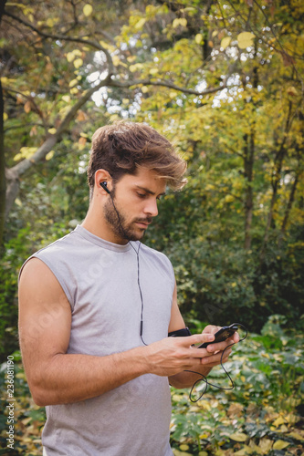 Closeup of one young athlete man preparing his smart phone on a path in the park during autumn.