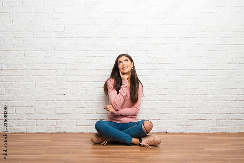 Teenager girl sitting on the floor in a room thinking an idea while looking up Teenager girl sitting on the floor in a room thinking an idea while looking up