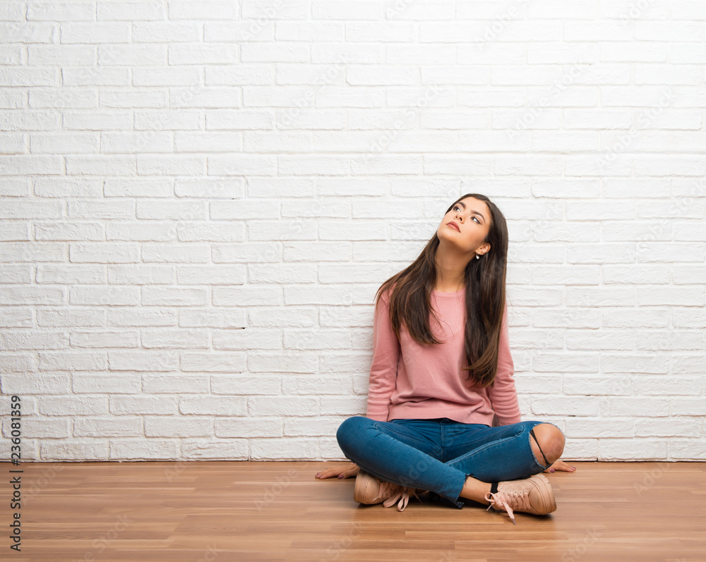 Teenager girl sitting on the floor in a room looking up with serious face Teenager girl sitting on the floor in a room looking up with serious face