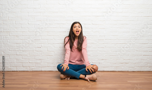 Teenager girl sitting on the floor in a room with surprise and shocked facial expression