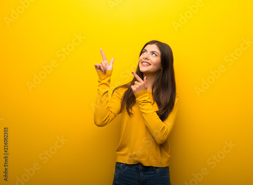 Teenager girl on vibrant yellow background pointing with the index finger and looking up