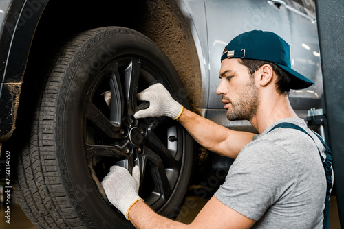 side view of auto mechanic in protective gloves checking automobile wheel at auto repair shop