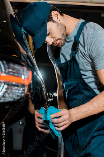 young auto mechanic cleaning car with rag at auto repair shop