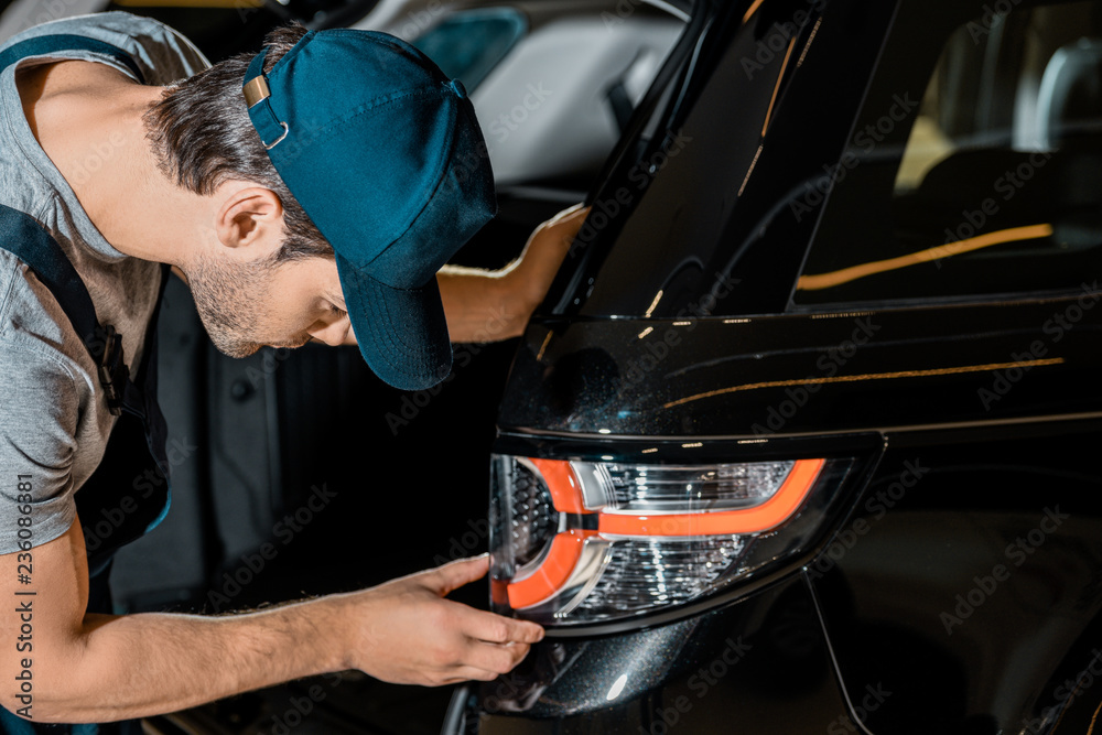 side view of young auto mechanic checking car back headlamp at auto repair shop