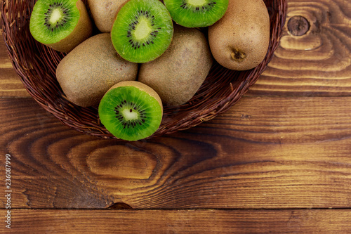 Kiwi fruits in wicker basket on wooden table. Top view
