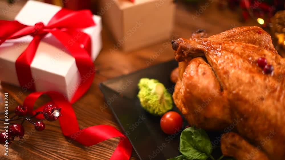 Christmas dinner. Roasted chicken on holiday table, decorated with candles and gifts. Delicious steamed roast turkey over wooden background. 4K UHD video footage 3840X2160