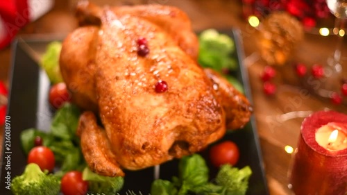 Christmas dinner. Roasted chicken on holiday table, decorated with candles and gifts. Delicious steamed roast turkey oover holiday blinking background. 4K UHD video footage. Slow motion 3840X2160 photo