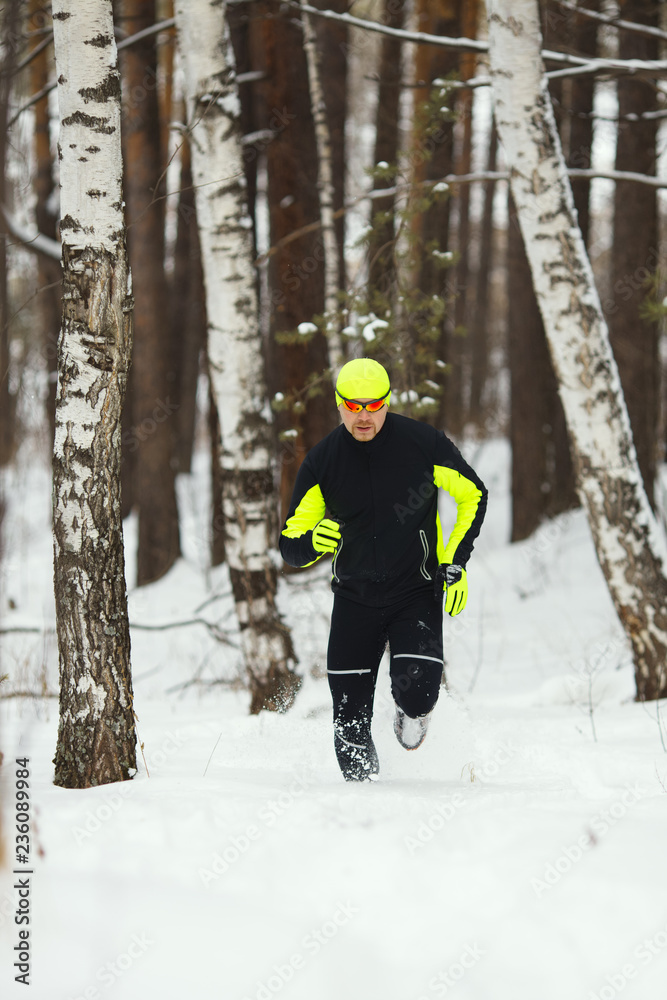 An athlete in sports clothes runs in a snow-covered forest.