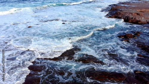 Side, dolley type drone footage of small waves and white-wash crashing over rocks at the beach in Australia, NSW. photo