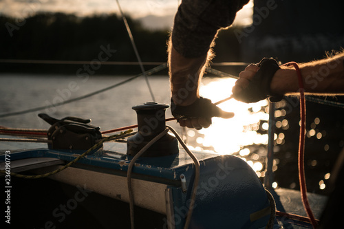 Silhouette of a sailors hands on a winch rope on a sailboat on a sunset. Shot with a selective focus.