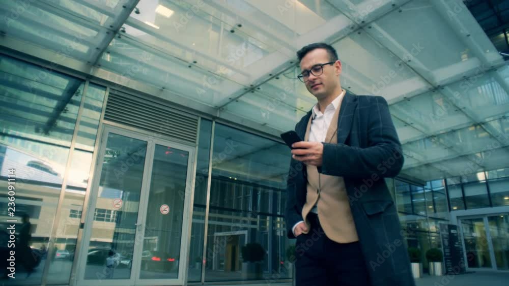 Businessman works with his phone while walking on a street, close up.