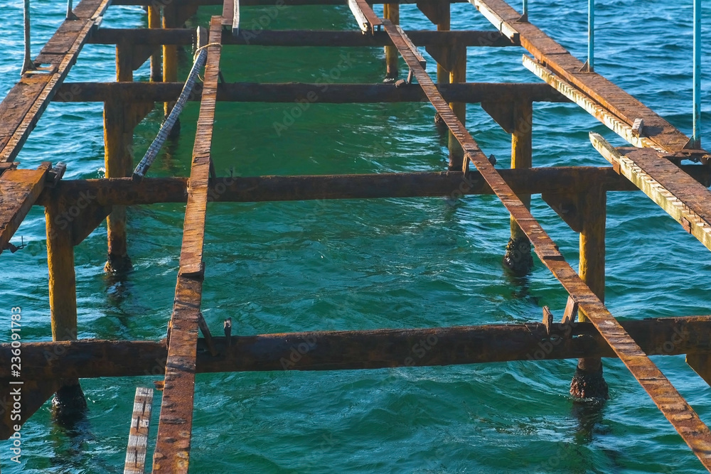 Destroyed old wooden pier on the sea. Rusty steel frame, repair.