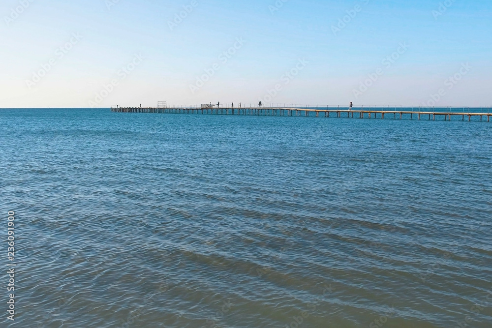 People are walking on old wooden pier in the sea. Side view. People are walking on old wooden pier in the sea. Side view.