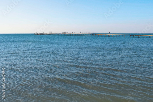 People are walking on old wooden pier in the sea. Side view. © familylifestyle
