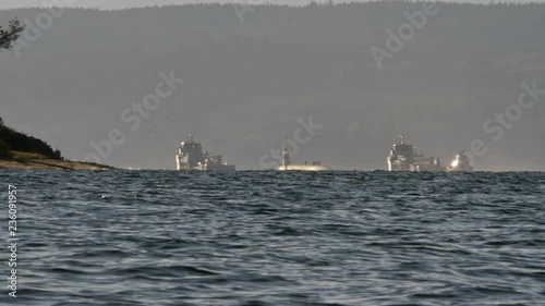 In the distance, a small Naval convoy travels Puget Sound, the ships and submarine are illuminated by the sun. photo