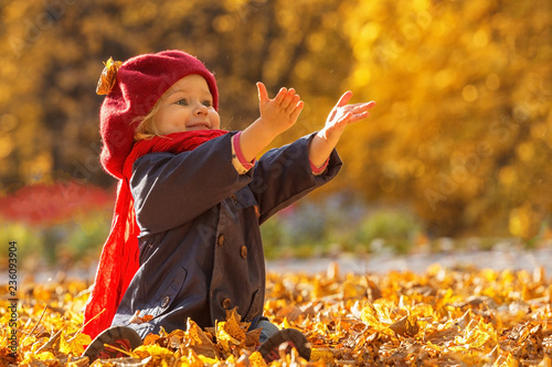 Happy autumn. A little girl in a red beret is playing with falling leaves and laughing.