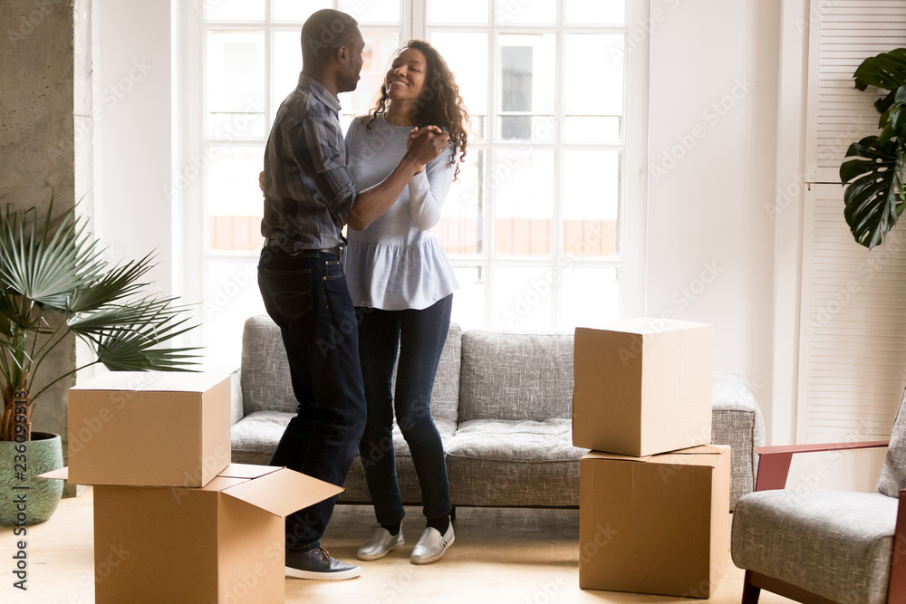 Happy African American couple in love dancing after moving in new house, attractive smiling woman and man celebrating relocating, cardboard boxes with belongings, homeowners in new apartment Happy African American couple in love dancing after moving in new house, attractive smiling woman and man celebrating relocating, cardboard boxes with belongings, homeowners in new apartment