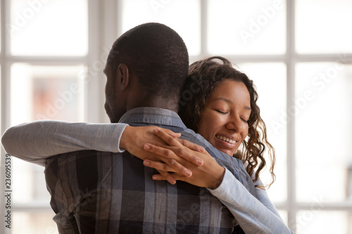 Attractive loving African American girlfriend embrace boyfriend, standing at home with closed eyes, affectionate couple in love romantic relationship, wife supporting husband rear view, gratefulness photo