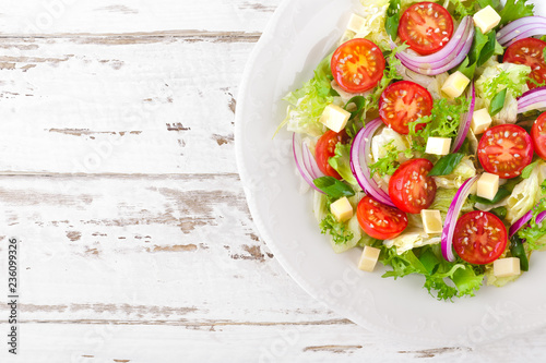 Fresh vegetable salad with tomatoes, lettuce, onion and cheese on white wooden background. Healthy vegetarian food. Top view