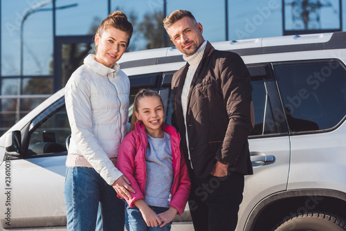  Preteen daughter standing with mom and dad near car