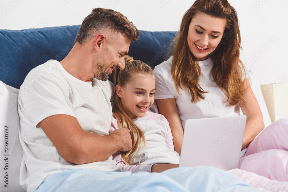 Obraz premium Smiling family lying in bedroom with laptop