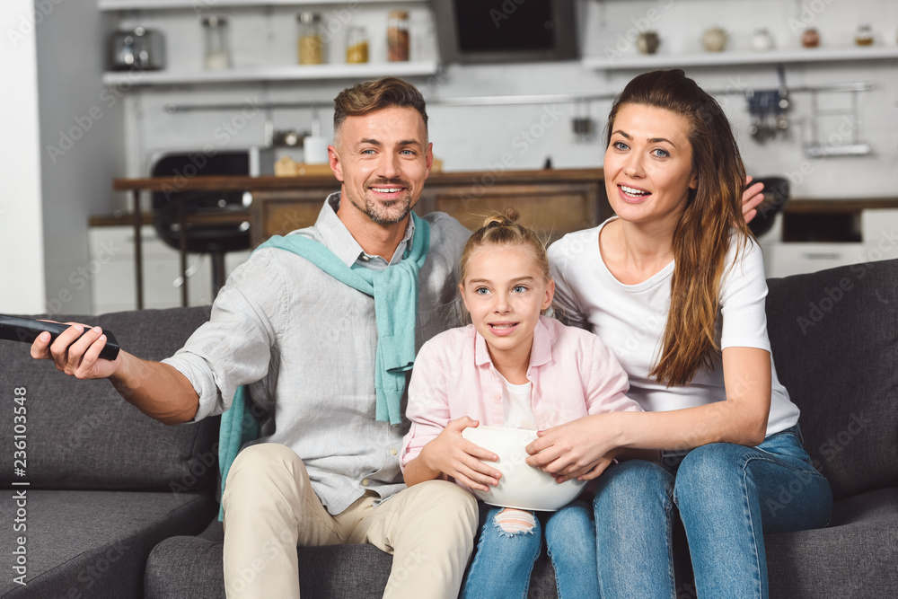 daughter eating popcorn from bowl while watching tv with parents daughter eating popcorn from bowl while watching tv with parents