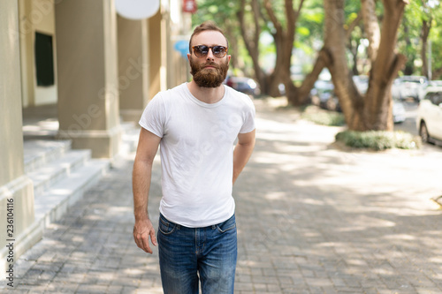 Focused handsome hipster guy enjoying weekend or vacation. Young man in sunglasses walking down summer street . walking outdoors concept © Mangostar