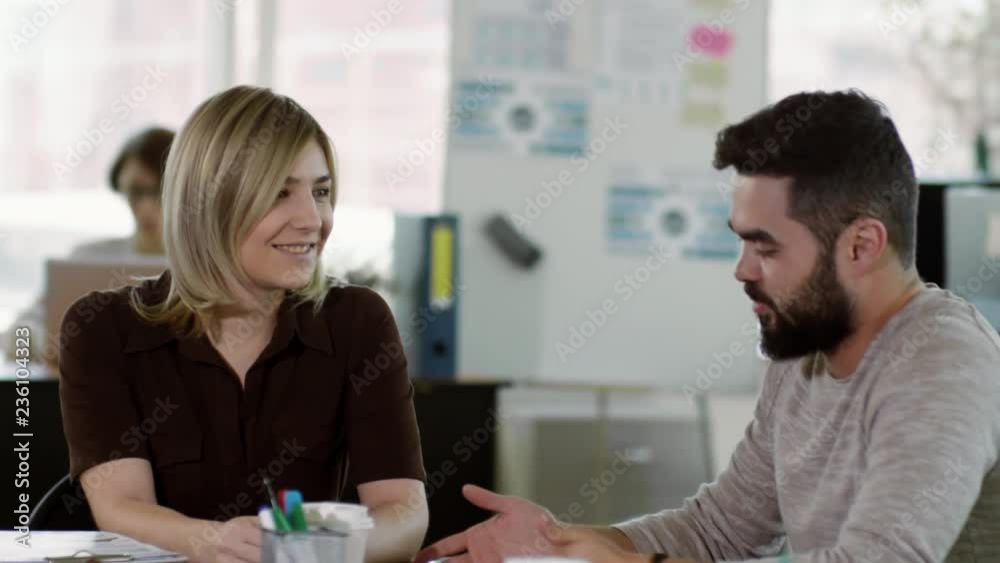 Tilt down of young caucasian woman and middle eastern man sitting at desk in the office and chatting Tilt down of young caucasian woman and middle eastern man sitting at desk in the office and chatting