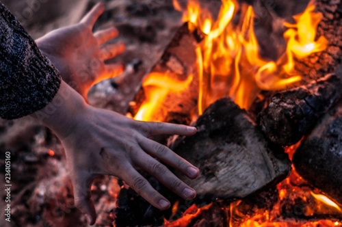 Obraz na plátně Man is keeping his hands close to a bonfire in the evening, view from top