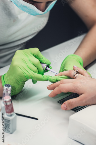 Professional manicure master in green gloves making manicure in salon
