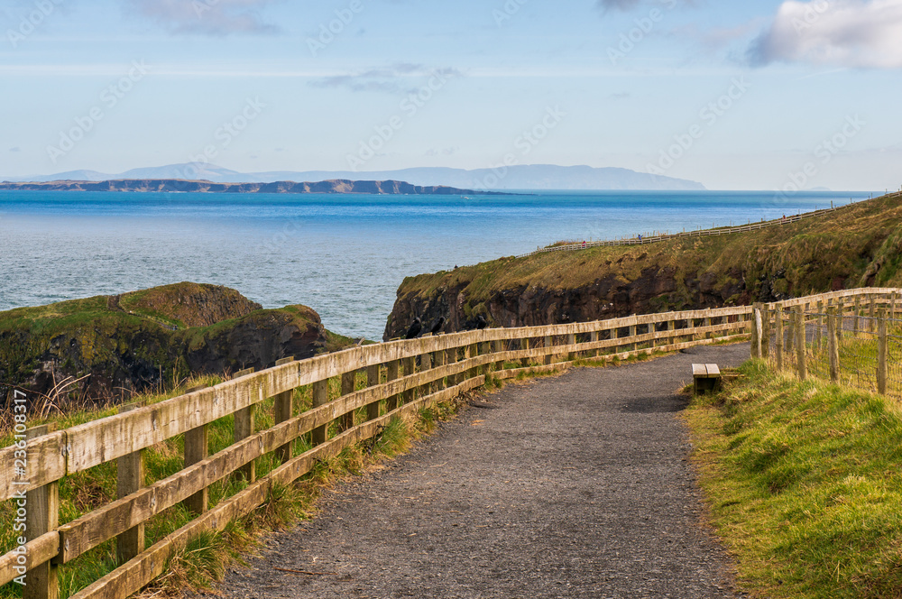 Irish landscape in County Antrim, well known touristic destination in Northern Ireland. Road to Carrick-a-rede rope bridge on a sunny winter day. Bench with a view. Irish landscape in County Antrim, well known touristic destination in Northern Ireland. Road to Carrick-a-rede rope bridge on a sunny winter day. Bench with a view.